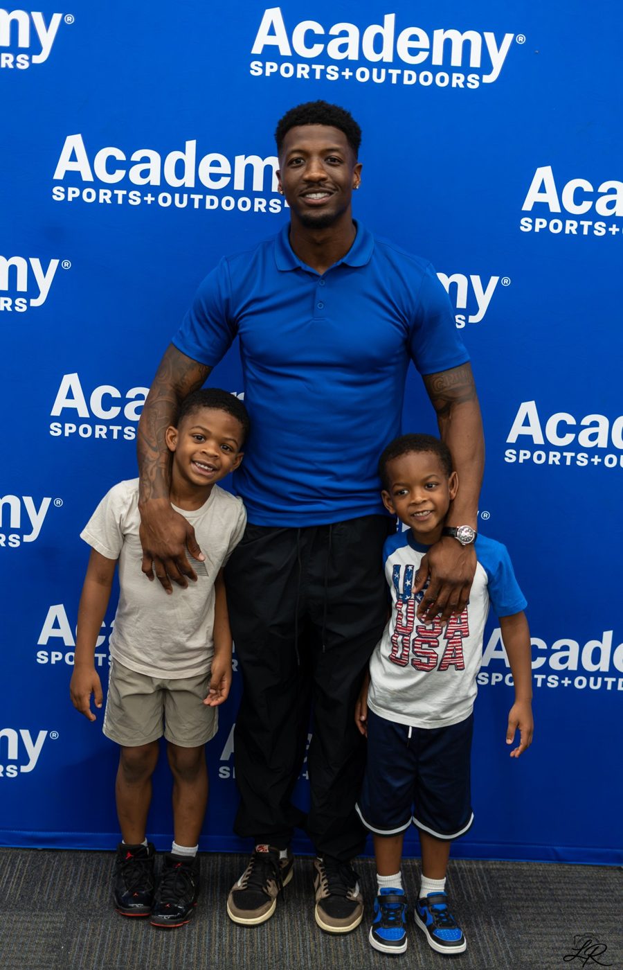 Anthony Miller II posing with two young children at the backdrop